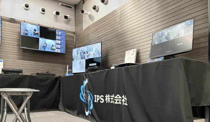 福岡オフィスのショールーム。IPS株式会社のクロスを掛けた机にモニターと録画機、奥の壁にカメラと大型モニター