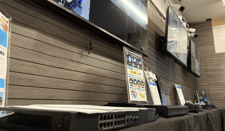 福岡オフィスの展示台の寄り。手前にLANの差し込み口が並ぶネットワーク機器、奥に説明のパネルと録画機