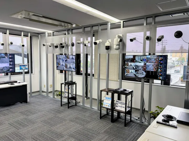 福岡オフィスのショールームの全景。金属の格子の展示棚の上段にカメラが並び、2台のモニターに映像、その下に録画機を置いた台