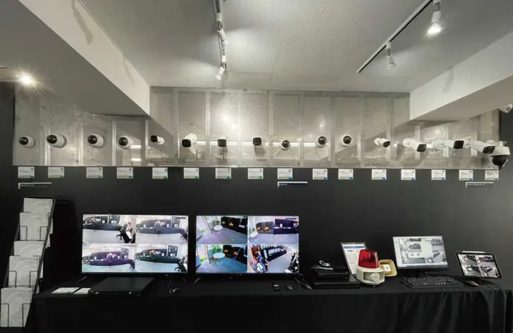 東京オフィスのショールームの展示の壁。パンチングメタルの壁にカメラが一列に並び、下のモニターに室内の映像が分割で映っている