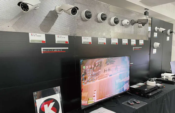東京オフィスの展示の壁。KSシリーズのAHDカメラが並び、下の長机に大型モニターと録画機が置かれている