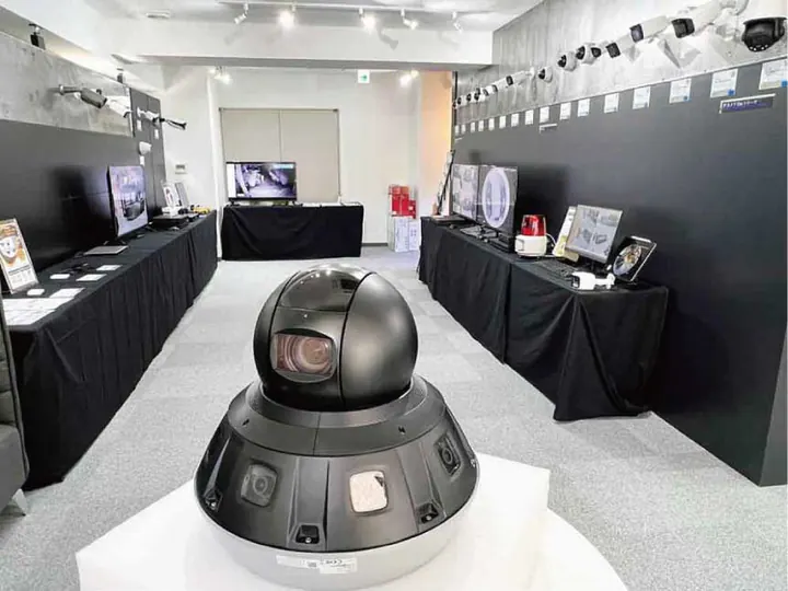 東京オフィスのショールーム。部屋の中央の台に黒い大型のカメラが置かれ、両側の長机にモニターと録画機が並ぶ